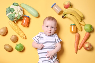 Cute little child with ingredients and purees in jars on color background, top view. Baby food