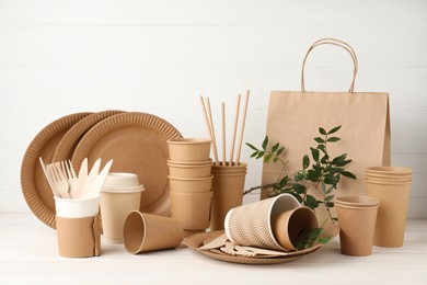 Photo of Eco disposable tableware and green twigs on white wooden table