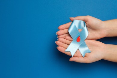 Woman holding light blue ribbon with paper blood drop on color background, top view and space for text. Diabetes awareness