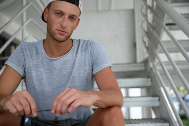 Handsome young man in stylish cap sitting on stairs outdoors. Space for text