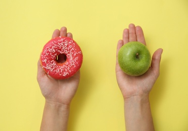 Top view of woman choosing between doughnut and healthy apple on yellow background, closeup