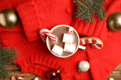 Flat lay composition with cup of tasty cocoa, candy cane and Christmas decor on wooden table, flat lay