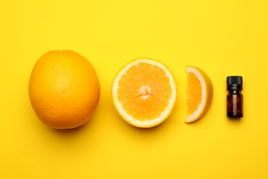 Bottle of citrus essential oil and fresh oranges on yellow background, flat lay