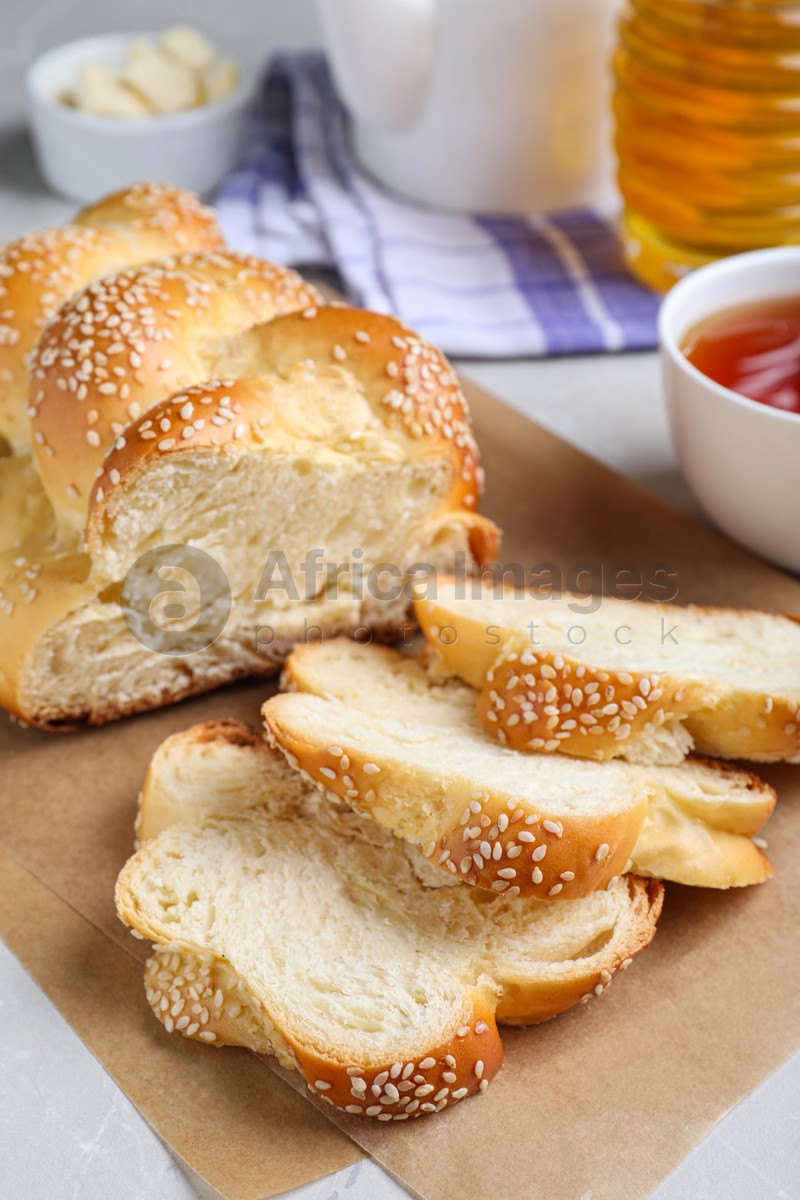 Photo of Cut homemade braided bread and freshly brewed tea on light grey table, closeup. Traditional Shabbat challah