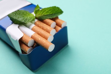 Pack of menthol cigarettes and mint on turquoise background, closeup. Space for text