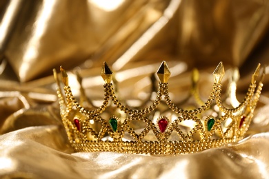 Photo of Beautiful ancient crown on golden fabric, closeup. Fantasy item