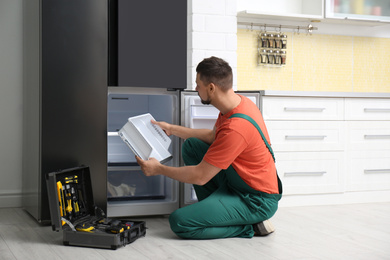 Professional male technician repairing broken refrigerator indoors