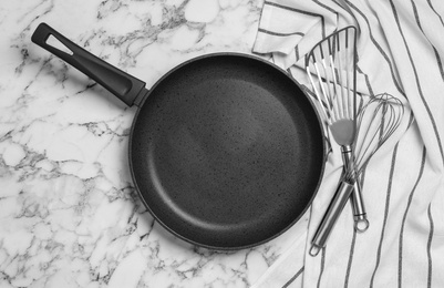 Frying pan, cooking utensils and tablecloth on white marble background, flat lay