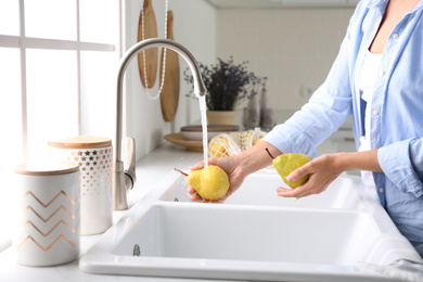 Woman washing fresh ripe pears in kitchen, closeup