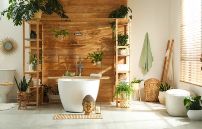 Stylish bathroom interior with white tub and green houseplants near wooden wall. Idea for design