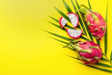 Delicious cut and whole white pitahaya fruits with palm leaf on yellow background, flat lay. Space for text