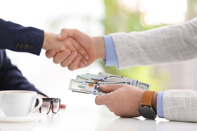Photo of Man shaking hands with woman and offering bribe at table in office