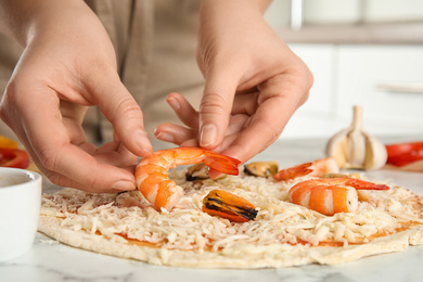 Photo of Woman adding shrimp to seafood pizza at white marble table, closeup