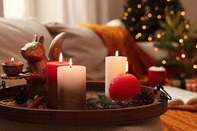 Tray with beautiful burning candles and Christmas decor on sofa at home