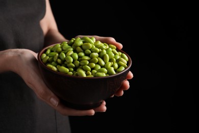 Woman holding bowl of edamame beans on dark background, closeup. Space for text