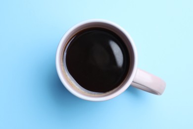 Fresh aromatic coffee in mug on light blue background, top view