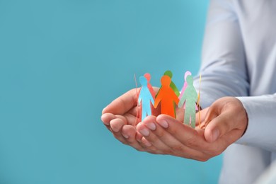 Photo of Man holding paper human figures on light blue background, closeup with space for text. Diversity and inclusion concept