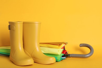 Pair of bright rubber boots near umbrella on pale orange background