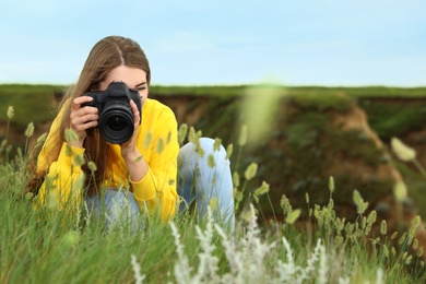 Female photographer taking picture of beautiful plants with professional camera on green hill