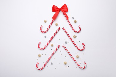 Christmas tree shape made of sweet candy canes and festive decor on white background, flat lay