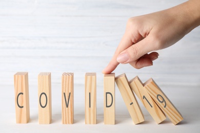 Woman stopping domino effect at white table, closeup. Prevent spreading of coronavirus