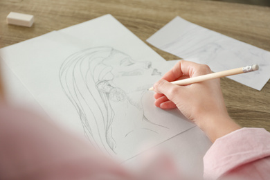 Woman drawing girl's portrait with pencil on sheet of paper at wooden table, closeup