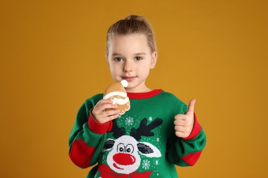 Cute little girl with Christmas gingerbread cookie on orange background
