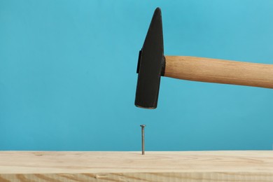 Hammering nail into wooden surface against light blue background, space for text