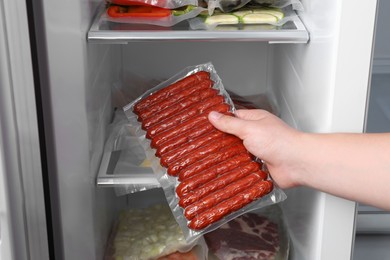 Photo of Woman putting vacuum bag with sausages into fridge, closeup. Food storage