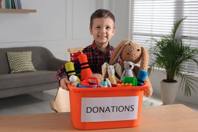 Cute little boy holding donation box with toys at home