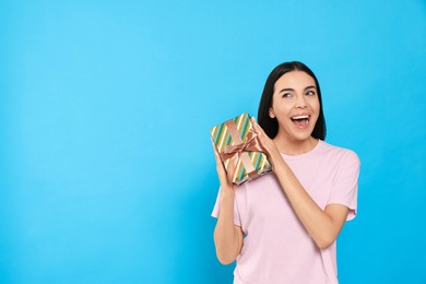Emotional young woman holding gift box on light blue background, space for text