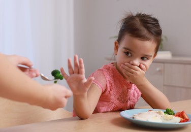 Cute little girl covering her mouth and refusing to eat breakfast at home