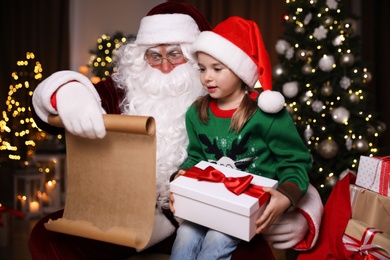 Photo of Little girl with Christmas gift near Santa Claus indoors
