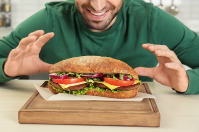 Hungry man and tasty sandwich on table, closeup
