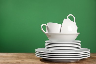 Photo of Set of clean dishware on wooden table against green background, space for text