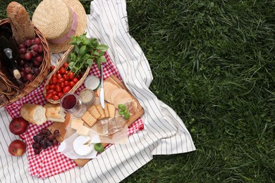 Picnic blanket with different products on green grass, top view. Space for text