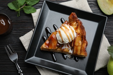 Photo of Slice of traditional apple pie with ice cream served on black wooden table, flat lay