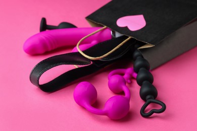 Shopping bag with different sex toys on pink background, closeup