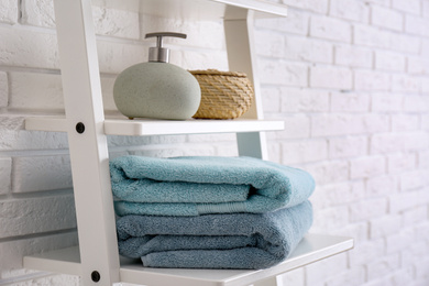 Clean soft towels and soap dispenser on shelves near white brick wall