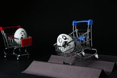 Egg with drawn scared face in shopping cart stunting on black background
