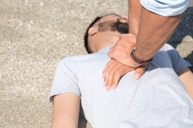 Passerby performing CPR on unconscious young man outdoors, closeup. First aid