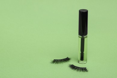 Photo of False eyelashes and tube of oil on light green background. Space for text
