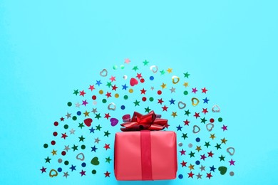 Red gift box and shiny confetti on light blue background, top view