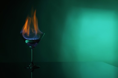 Cocktail glass with flaming vodka on green background, space for text