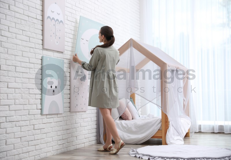 Photo of Decorator hanging picture on white brick wall. Children's room interior design