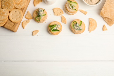 Delicious crackers with humus and cucumber on white wooden table, flat lay. Space for text