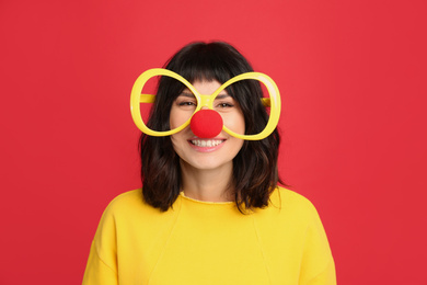 Joyful woman with large glasses and clown nose on red background. April fool's day