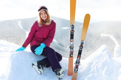 Young woman with ski equipment sitting on snowdrift in mountains. Winter vacation
