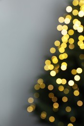 Blurred view of beautiful fir tree with Christmas lights on grey background, space for text