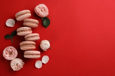 Delicious macarons and roses on red background, flat lay. Space for text